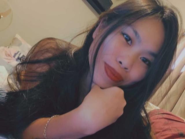 ButterCups has long black hair, red lipstick, and is resting her chin on her hand, smiling with blue eyes, wearing a black top and a silver bracelet.