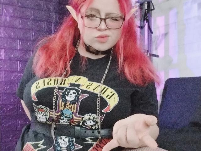 ChubbyLeahPearl with red hair, elf ears, glasses, black choker, black t-shirt, pointing, holding wallet, large tits, cute, purple wall in background, slightly pouty expression, medium skin.