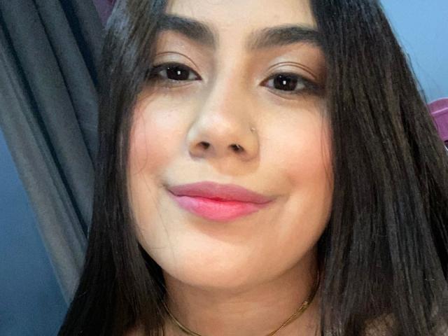 CurvyBuff has medium brown skin, dark brown eyes, and pink lipstick. She has straight, dark brown hair, a gold nose ring, and a gold necklace. She's smiling softly.