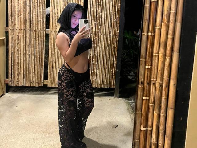 NicoleAnniston with black lace headscarf, black lace bra, and black lace pants, standing in front of mirror, holding phone, showing midriff and small ass. Reflective bamboo walls.