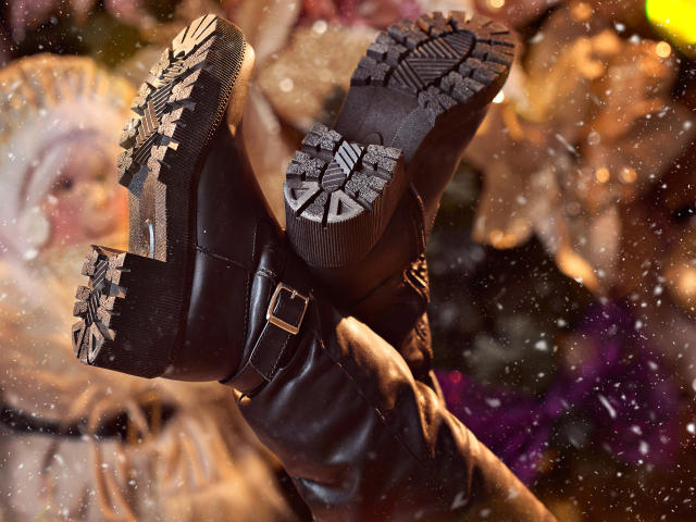 Las botas de cuero negro de RoseNichols tienen suelas con un diseño detallado de copos de nieve, que muestran los patrones texturizados y en relieve. Sus botas están ligeramente abrochadas y sus piernas están cruzadas en la foto..