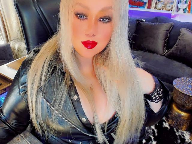 Etername-hot with long blonde hair, red lipstick, black leather jacket, and black lace sleeve, showing off her tits in a cozy room.