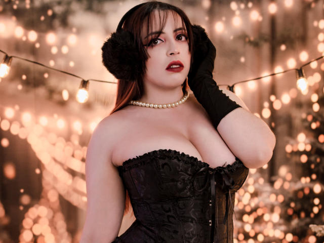 Rosalinnes with big boobs in a black, strapless corset, black gloves, pearl necklace, and furry ear accessories, looking seductive with red lipstick and dark makeup. Glowing string lights.