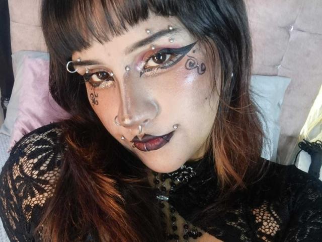 DanniLuke has multiple facial piercings, dark makeup, and black lace top. She's looking at the camera with a slight smile, showcasing her nose and facial piercings.
