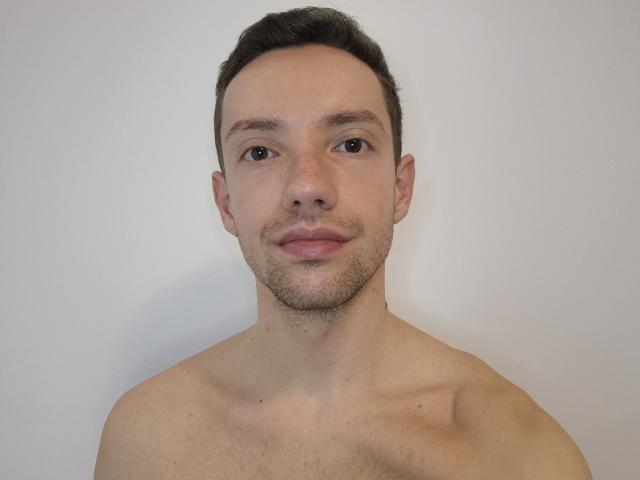 Cocco69 has a light skin tone, short dark brown hair, brown eyes, and a slight beard with a calm expression. He's shirtless with a clean, smooth chest.