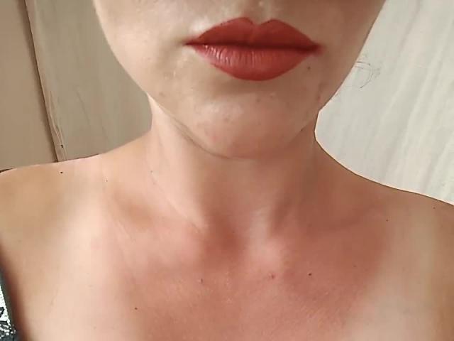 Farida69's face with red lipstick, slightly flushed skin, and visible collarbone. Boobs not visible, but bare shoulders. Her lips are plump and her skin is pale.