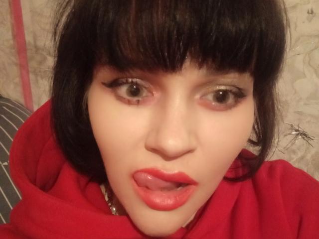 Farida69 has pale skin, black bob with bangs, brown eyes, red lipstick, and is sticking out her tongue. She's wearing a red hoodie.