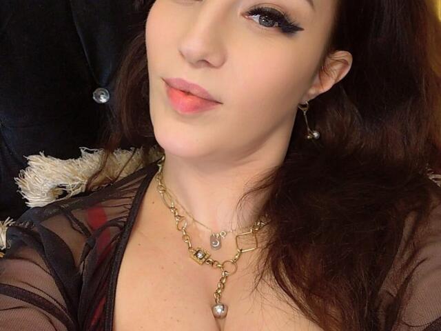 Vanessa, con labbra rosa carnose, eyeliner scuro e capelli castani ondulati, indossa una collana d'oro con un diamante e una maglietta nera trasparente che lascia intravedere il seno..