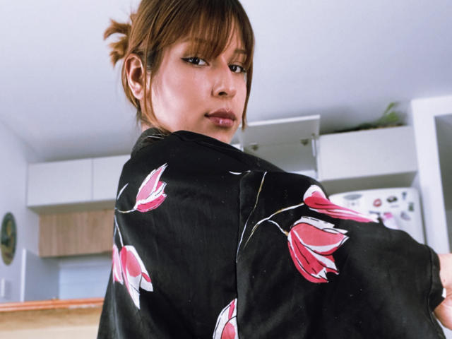 KiaraHernandezX with brown hair in a bun, wearing a black floral kimono, looking back over her shoulder, showing her ass, in a bright room.