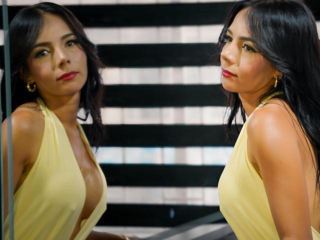 EvelinLuna with dark hair, red lipstick, yellow halter dress, showing her tits in a mirror, wearing gold hoop earrings, looking sexy, reflection of her face on the left.