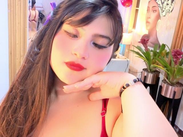 CataleyaHankl with red lipstick, brown hair, and closed eyes, resting her chin on her hand, wearing a red top, and a black bracelet, looking cute and relaxed.