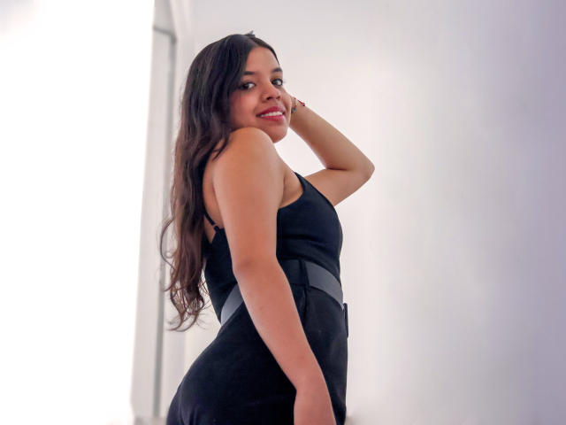 LiinaSantacruz with long dark hair, wearing a black dress, smiling, showing her back, hand in hair, standing, light skin, red lipstick, medium tits, slim, sexy.