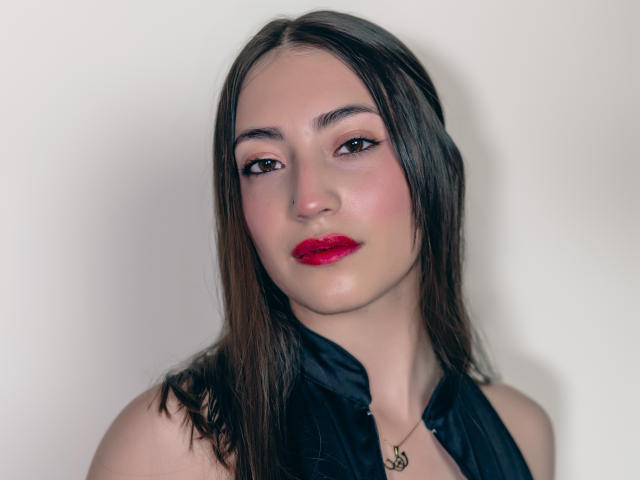 AnnFisher with wet brown hair, red lipstick, pink eyeshadow, and black halter top, showing off her ass-pretty face and a small nose ring. She's looking directly at the camera.