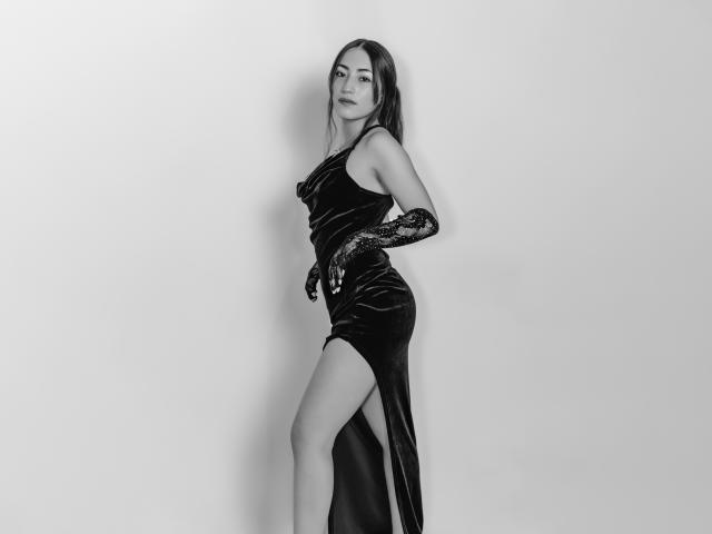 AnnFisher in a black velvet dress with a high slit, wearing black lace gloves, standing with one leg raised, showing her bare thigh, looking seductively at the camera.