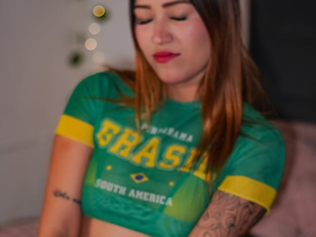 SophiaSth with brown hair, red lipstick, green Brazilian soccer shirt, yellow sleeves, tattoo on right arm, looking down, soft focus, green and yellow colors, cute, attractive.