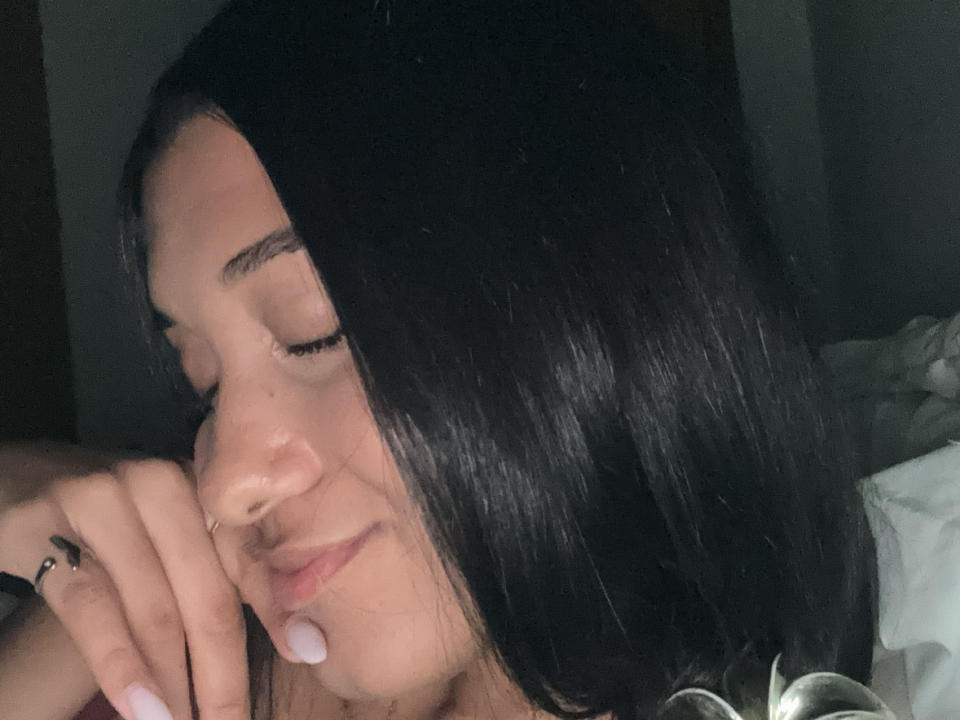 MilenaZ tem cabelos escuros e lisos, olhos fechados e uma pequena gota branca no queixo. Ela está com a cabeça apoiada na mão, com um sorriso suave..