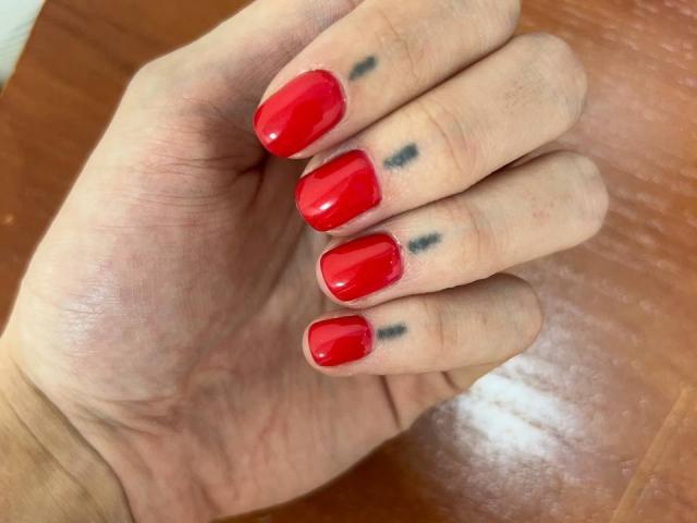 MoonLiza's hand with shiny red nail polish, small black tattoos on fingers, resting on a wooden surface. Boobs not visible. Ass, tits, pussy, none. Fingers slightly curled.