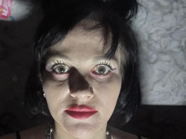 Farida69's face, with wide green eyes, black hair, red lipstick, and slightly flushed skin, looking directly at the camera, showing a slight sweat on her forehead.