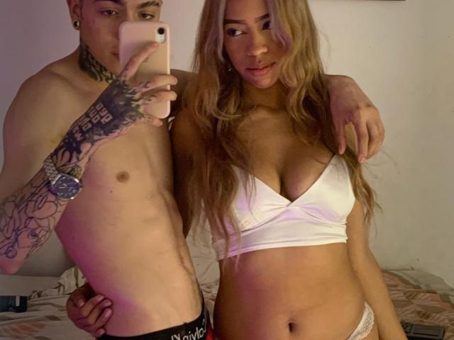 A selfie of IceCumHot with a tattooed dude holding a phone, and IceCumHot in a white bra, showing her tits and flat stomach. His arm's around her.
