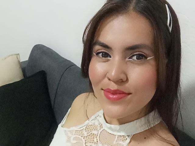 MonaLia69 with pink lipstick, brown eyes, white lace top, nose ring, and black headband, smiling at the camera, showing her cute face and soft, curvy features.
