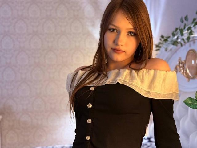 Bubochka has long brown hair, light skin, and is wearing a black off-shoulder top with white ruffle and buttons, looking at the camera with a subtle smile.