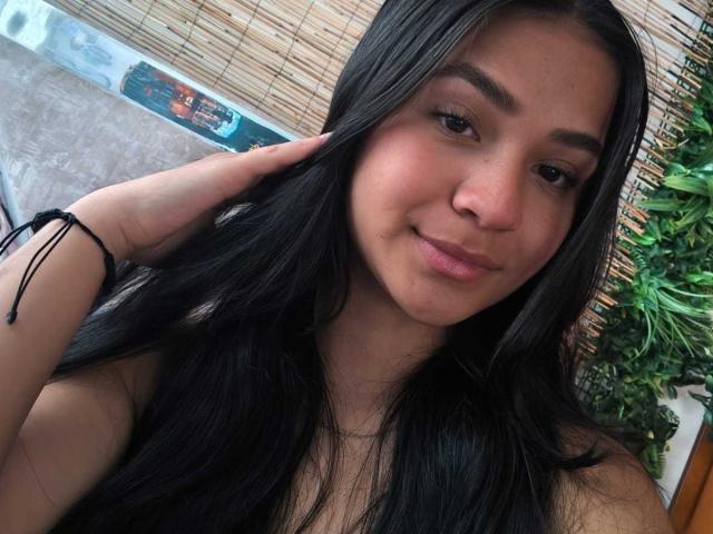 RouxiMori with long black hair, brown eyes, and a slight smile, touching her hair with a black bracelet on her wrist, showing her cute, small tits.