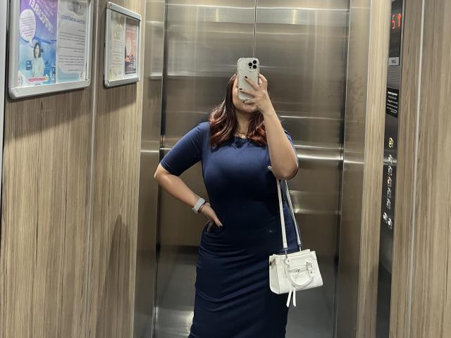 GabrielaFerrer with dark red hair, wearing a navy blue dress, white purse, and wristwatch, taking a selfie in a elevator, showing her curvy ass and medium tits.