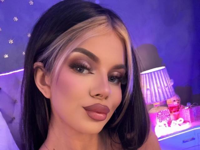 IvyRaven has blonde highlights in her black hair, full eyebrows, long eyelashes, and puffy pink lips. She's looking at the camera with a slight smile.