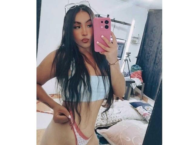 MissCharlottt with long black hair, light blue bra, and pink thong, pulling down pink thong to reveal her pussy, taking a mirror selfie with pink phone.