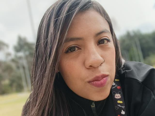 MeganFerrerr with brown hair, nose ring, black eyeliner, pink lipstick, and black jacket, pouting her lips slightly. Her cute face is centered in the shot.
