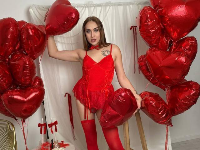 DawnGwin stands in red lingerie, holding red heart balloons, wearing a red choker, and red thigh-highs, showing her tits and a tattoo near her right breast.