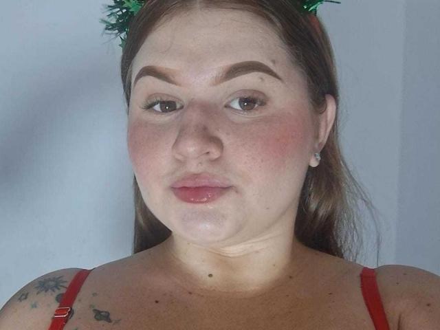 ValentinaDiazHot with red bra, green leafy headpiece, brown eyebrows, pink cheeks, small nose, slightly parted pink lips, tattoo on left shoulder, and brown hair, looking directly at camera.