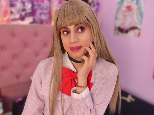 EimyFlorian with long blonde hair, pink eye makeup, red bowtie, white shirt, black choker, hand on cheek, pink lips, looking to the side, in a pink-tinted room.