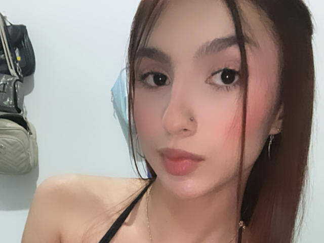 MilanMoon has light skin, brown eyes, and straight brown hair, wearing a black halter top, with a nose piercing, and subtle pink lips, looking at the camera.