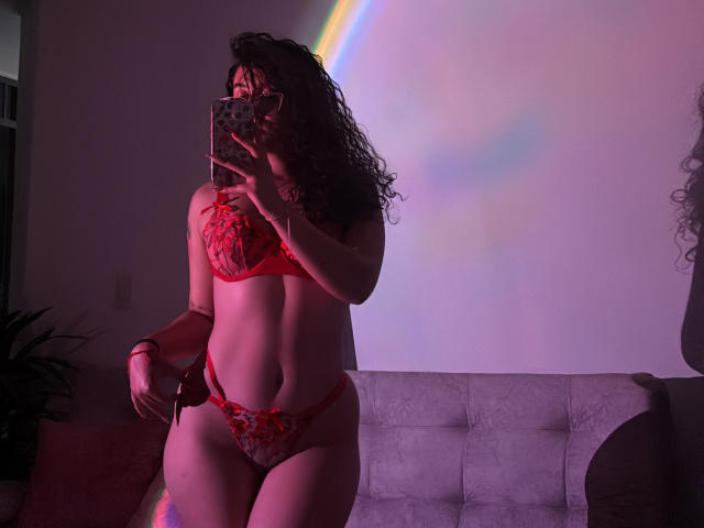 SophiaBrowm with wet black hair, wearing a red, long-sleeve, cut-out, mesh bodysuit, showing her ass and a tattoo on her right shoulder, taking a mirror selfie.