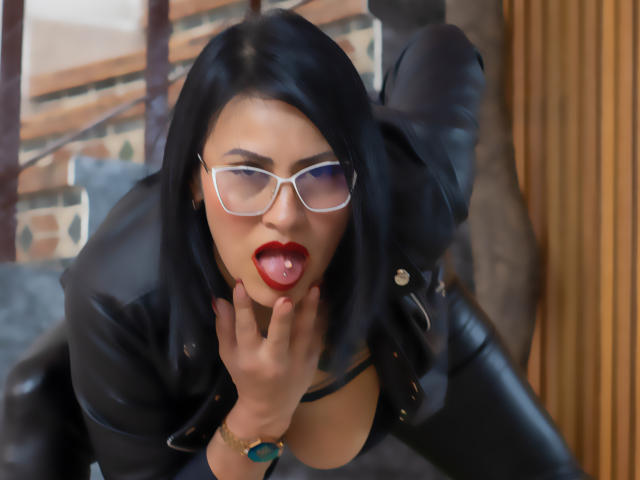 Donna Jones, com cabelo preto, batom vermelho e óculos, língua de fora, mão no pescoço, jaqueta de couro preta, decote visível, olhando para cima, relógio azul, sexy, provocante..
