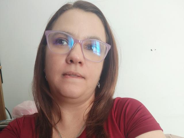 AmeliaWilson has brown hair, purple glasses, and a serious expression. She's wearing a red shirt and a necklace, with visible eyebrows and slightly parted lips.