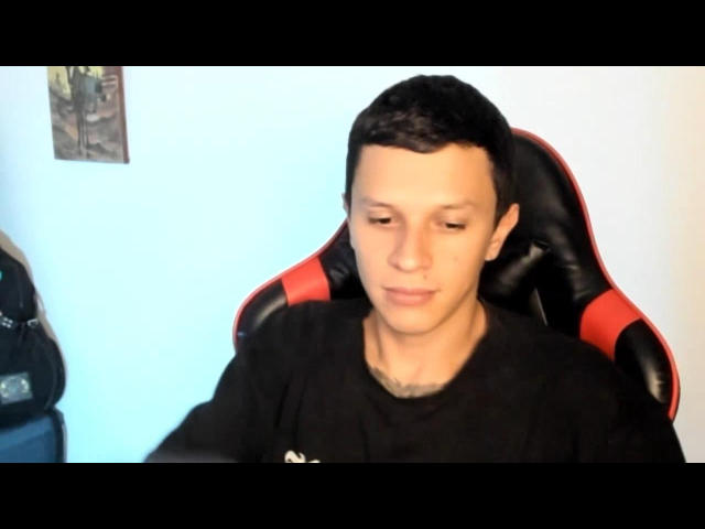 MasterDaveExtreme with short black hair, wearing a black shirt, sitting in a red and black gaming chair, looking down with a neutral expression.