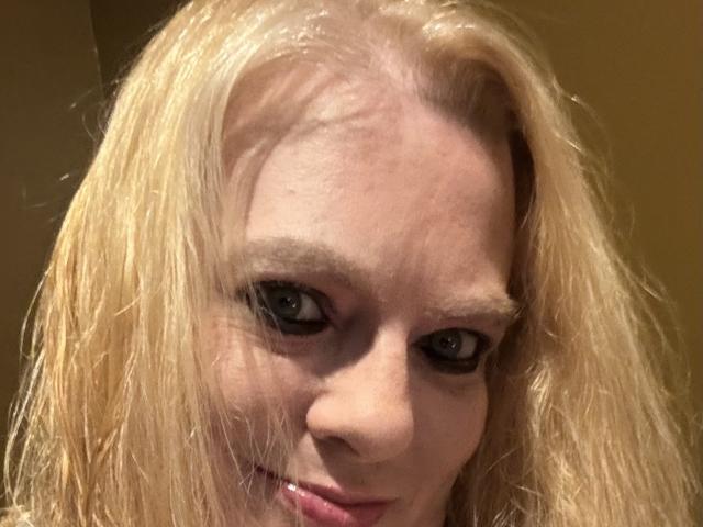 Cherish Williams tem cabelos loiro-escuros, levemente úmidos, pele clara e olhos azuis. Ela está olhando para a câmera com um sorriso discreto, mostrando uma pequena protuberância no nariz..