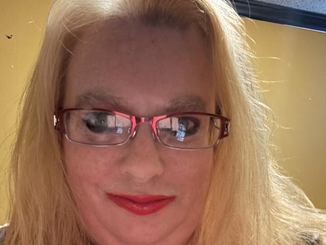 Cherish Williams tiene el cabello rubio, gafas rojas y lápiz labial rojo. Sus ojos azules miran ligeramente hacia un lado, y está sonriendo con sus labios rojos. Su rostro está centrado..