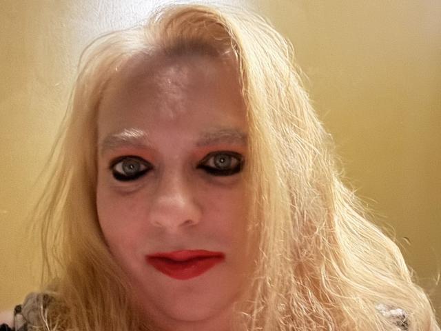 Cherish Williams tem cabelo loiro, olhos azuis e batom vermelho. Ela está olhando diretamente para a câmera com um leve sorriso, usando delineador preto. Seu rosto está levemente suado..