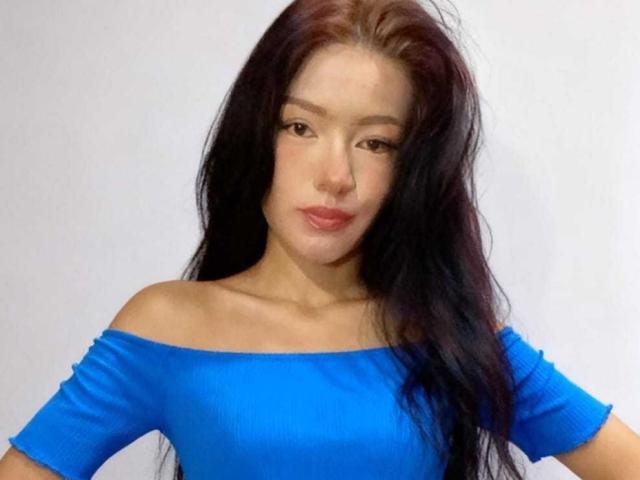 IvorySelene with long black hair, wearing a bright blue off-shoulder top, has small tits and a cute face, looking straight at the camera with slightly pouted lips.