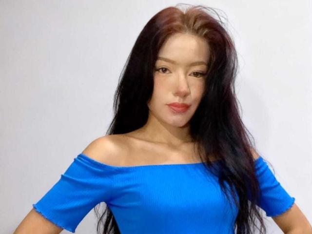 IvorySelene has long black hair, a cute face, and is wearing a blue off-shoulder top, showing her small tits and smooth skin.