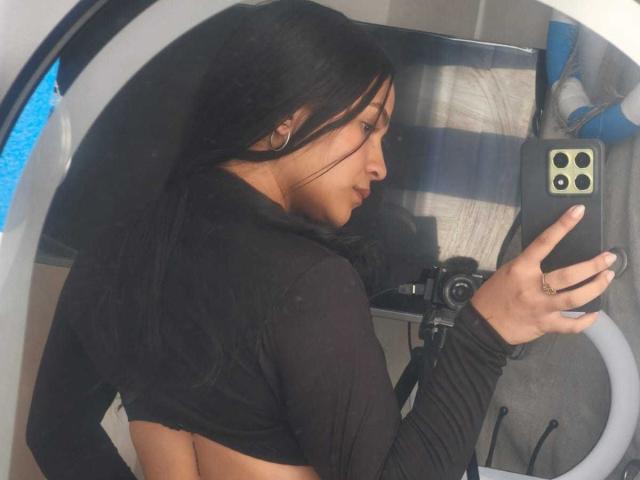 RouxiMori with long black hair, wearing a black long-sleeve top, showing her back and a small butt, taking a selfie with a ring on her finger, in a mirror.