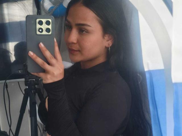 RouxiMori with long black hair, wearing a black long-sleeve top, holding a phone, taking a selfie, showing her face and small hoop earrings, looking at the camera.