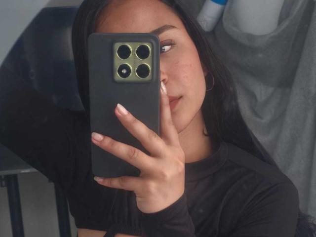 RouxiMori with long black hair, wearing a black shirt, holding a green iPhone, taking a mirror selfie, showing her nose and slightly parted lips. Her nails are manicured.