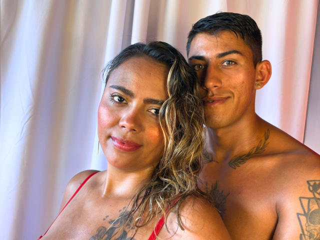 FuegoYSeduccion, une femme latina aux cheveux blonds et au rouge à lèvres rouge, se tient nue, ses seins visibles, à côté d'un homme latino musclé, tatoué, dont les fesses sont légèrement en arrière..