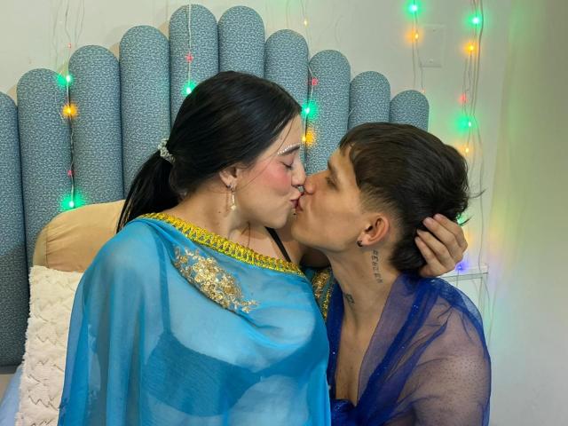 AnjaliRohan with black hair in a blue and gold saree, kissing a brown-haired man in a blue sheer top. Her tits are visible, his hand is on her ass.
