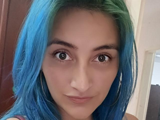 KarolLove69 has blue-green hair, brown eyes, and a slight smile. She's wearing large hoop earrings, and her makeup is subtle. Her nose is small and her skin is fair.