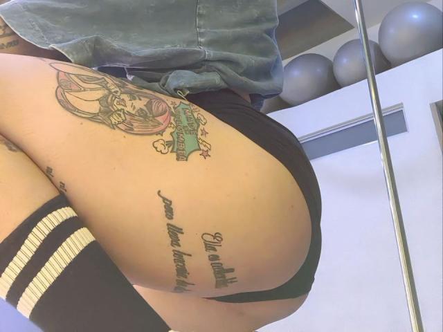 YeiSela's tattooed ass in black shorts, showing a colorful tattoo on her thigh and cursive script on her butt. She's wearing a denim shirt and striped knee socks.
